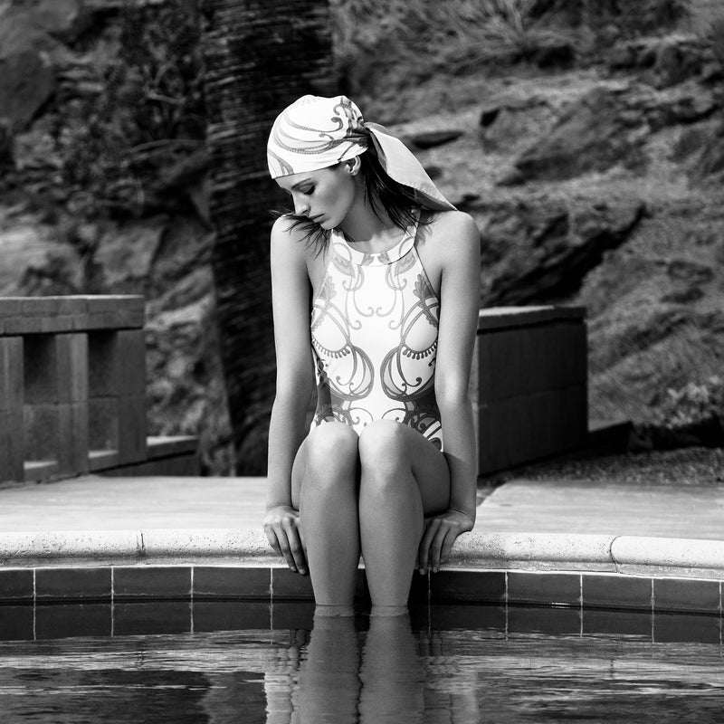 woman sitting by the pool wearing an olympic one-piece swimsuit and a bandana