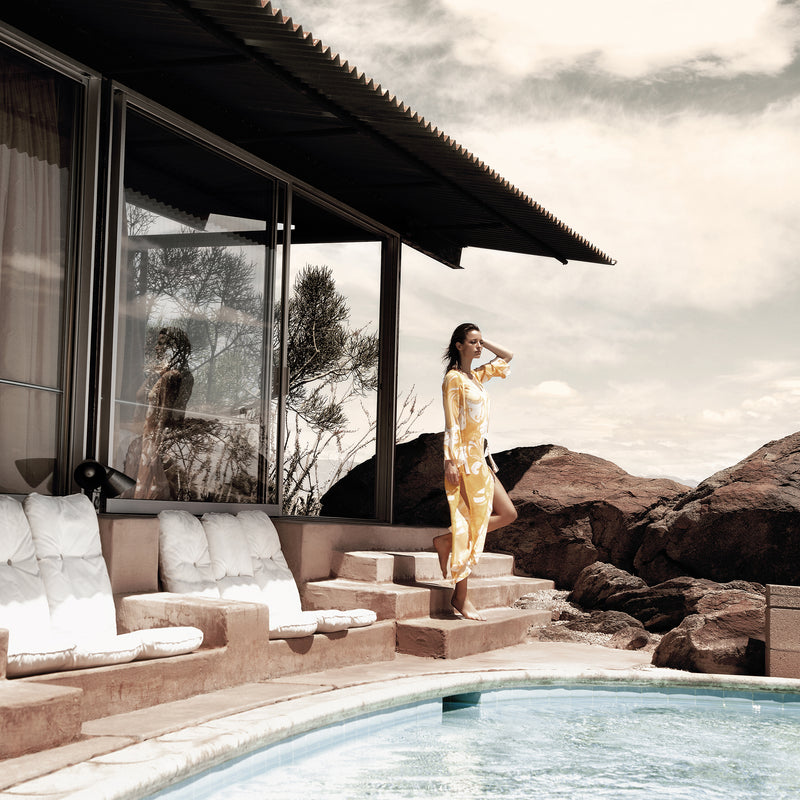 woman by a pool in palm springs wearing a silk kaftan in a yellow paisley print